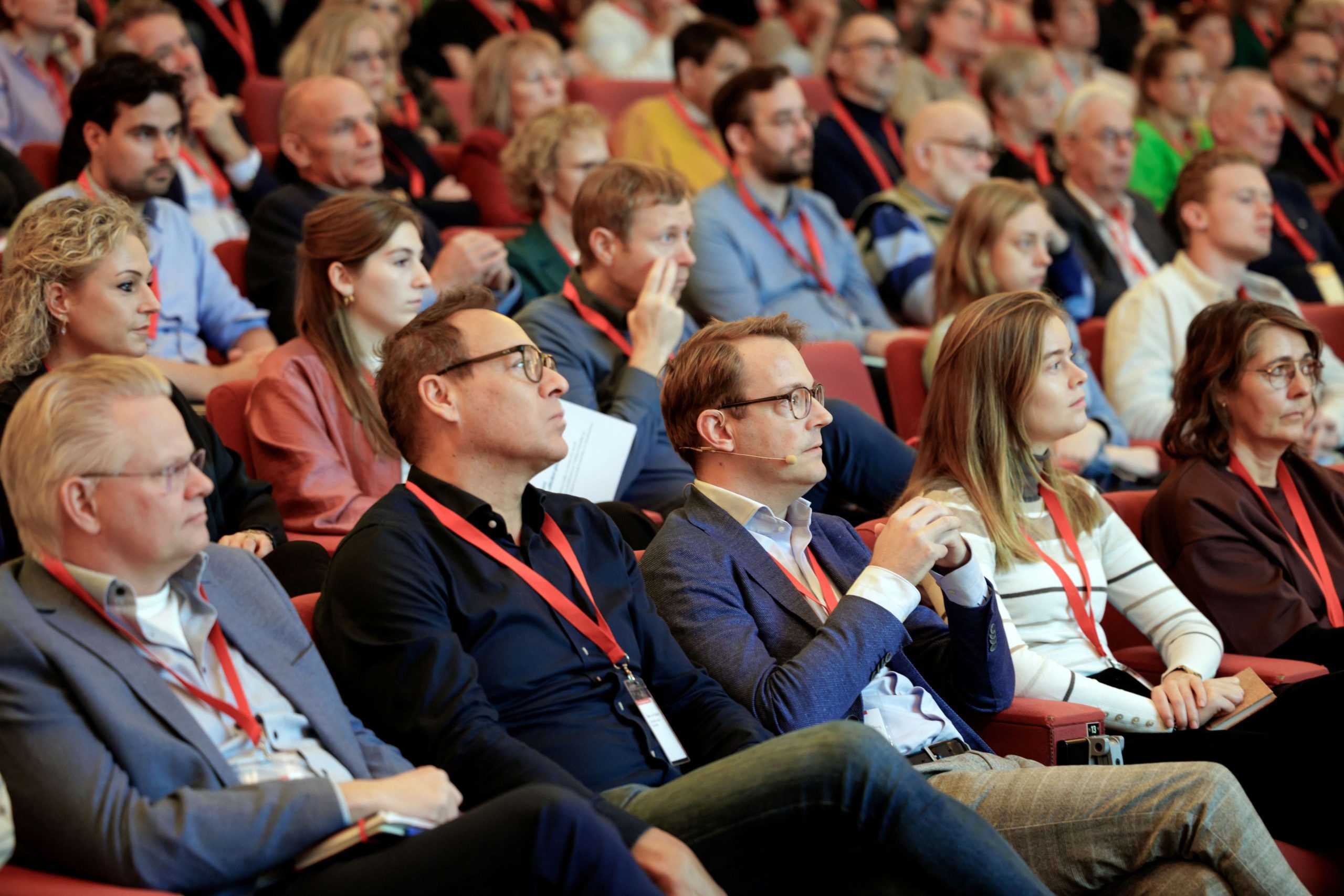 Publiek aanwezig zittend op rode stoelen bij BACB-sessie op de Dag van het Wonen