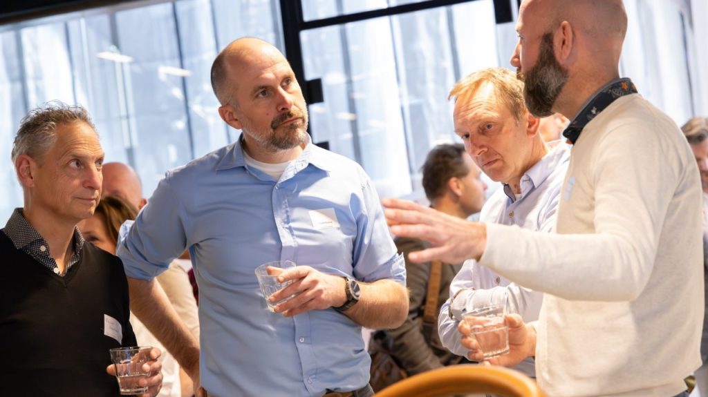 Drie mensen zakelijk staand in gesprek in een ruimte