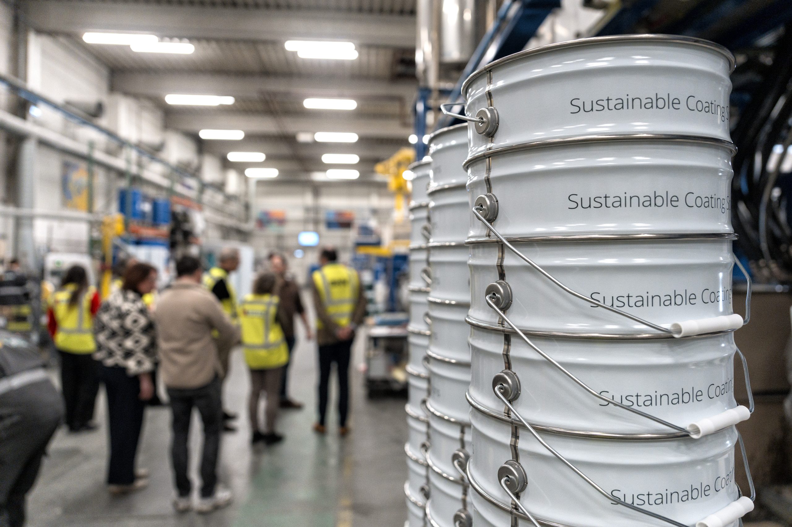 Bezoek van gedeputeerde Martijn Van Gruijthuijsen aan Baril Coatings, lopend in de hal, blikken verf met tekst sustainable te zien.